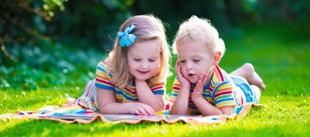 Two kids lying on the grass reading